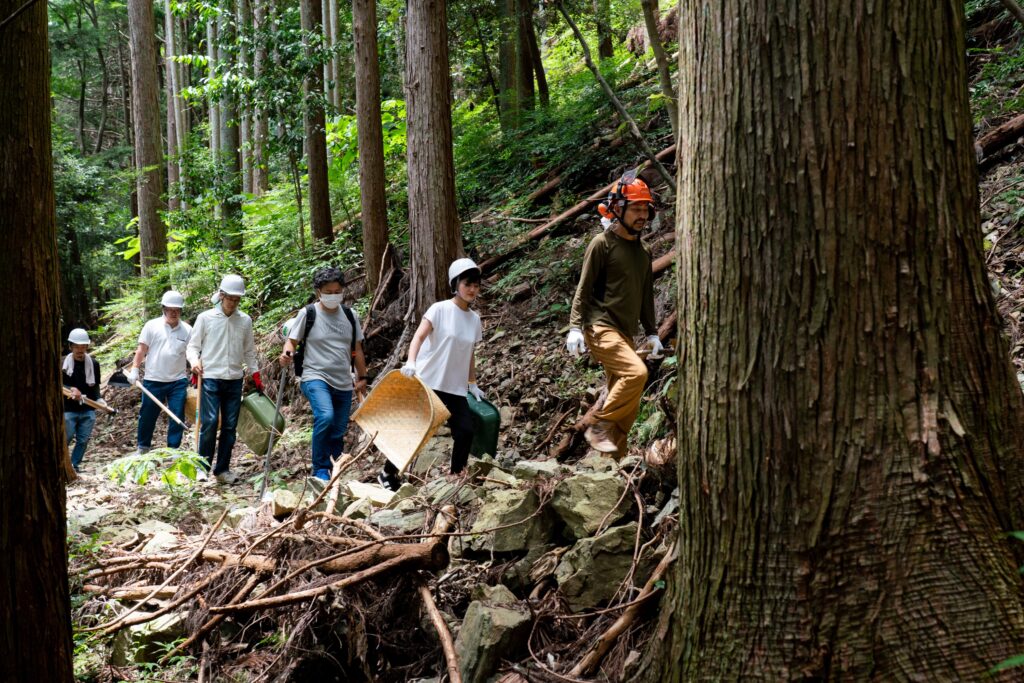 道づくりの道具を手にして林道を歩く木こり隊